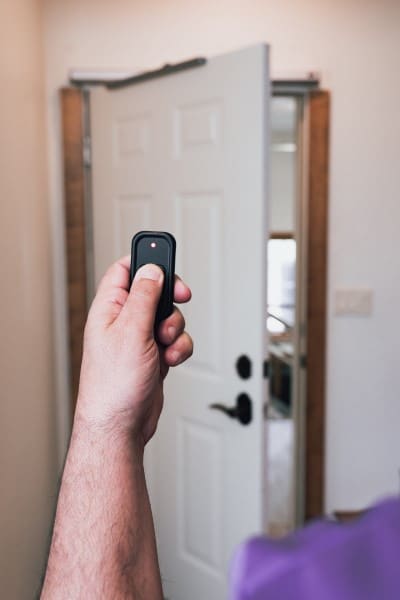 a closeup of a remote in hand opening a storm door in a home