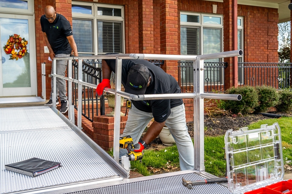 A crew in uniform installing a wheelchair ramp outside of a homeowner's front door