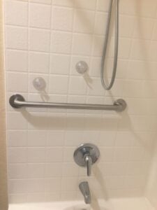 Horizontal silver grab bar installed above a tub faucet on a white tiled wall.