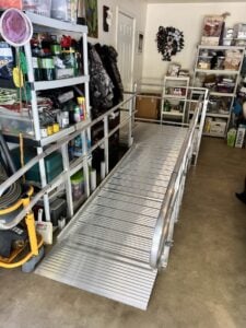 Aluminum modular ramp with handrails installed inside a cluttered garage leading to an interior doorway.