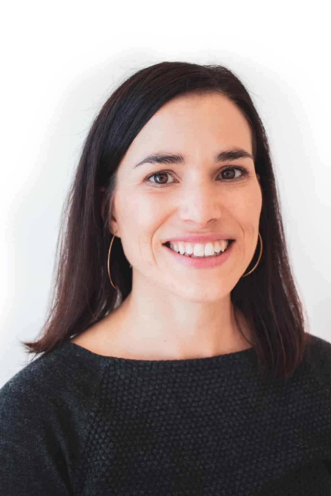 Headshot of a smiling woman with dark hair and large gold hoop earrings against a plain white background.