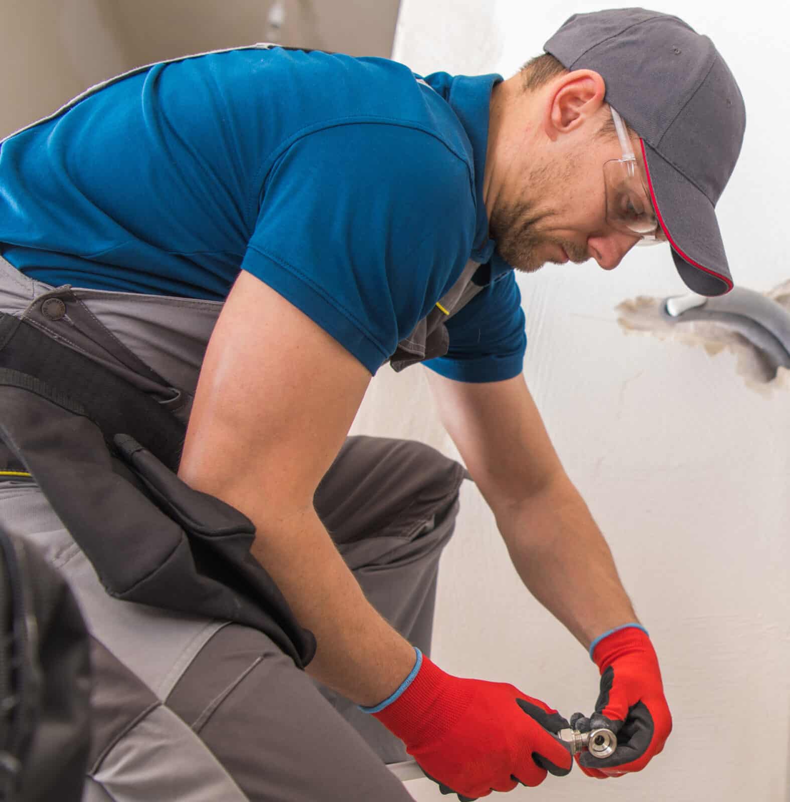 man in a uniform installs plumbing into a hole in the bathroom wall