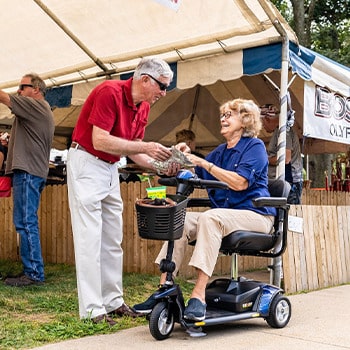 Woman sits on motorized scooter looks at a brochure with a standing man in red