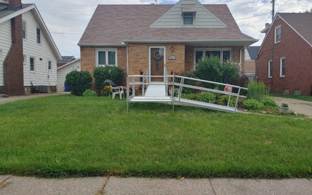 L-shaped modular aluminum ramp system with mesh decking leading to a residential home entrance with light siding.