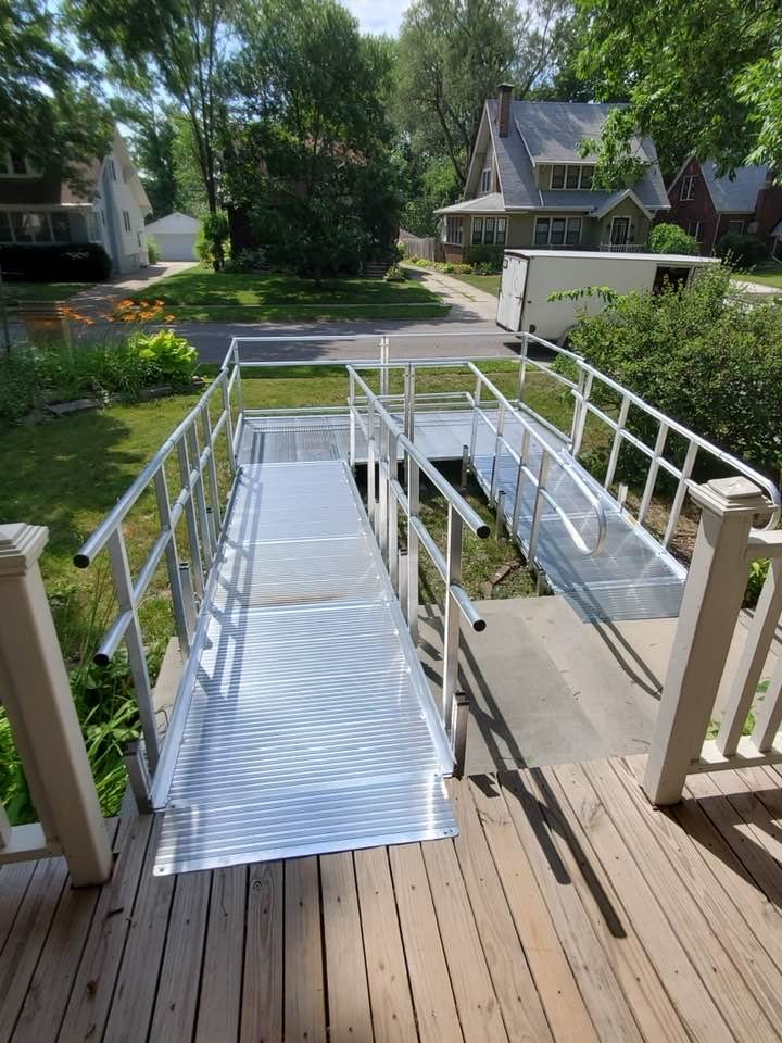 Two modular aluminum wheelchair ramps descend from a wooden porch in a residential setting.