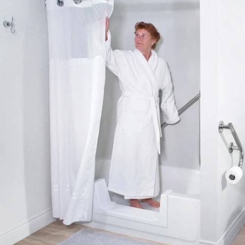 Woman in bathrobe stands in a walk in tub and slides the curtains open