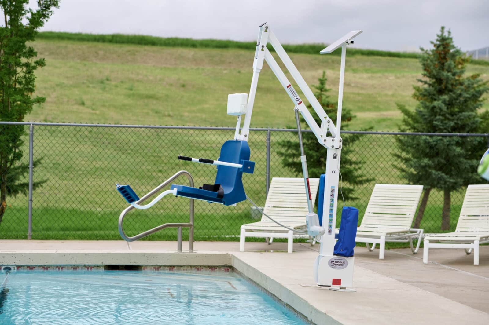 a distant shot of a white and blue pool lift installed and hanging over the pool