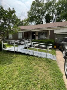 Long, modular aluminum wheelchair ramp with railings leading up to the front door of a brick and brown house.