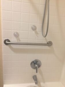Horizontal stainless steel grab bar and bath faucet on a white tiled shower wall, with two suction cups above.