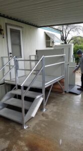 Aluminum stairs and landing with railings leading to a white door, with a vertical platform lift beside it.