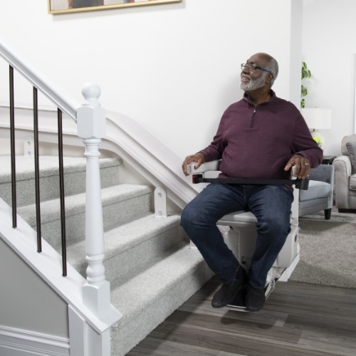 man sits in a chair lift on the wall at the bottom of the stairs in his home