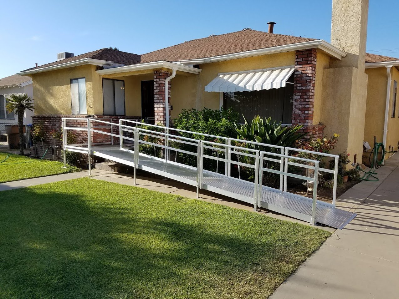 Metal accessibility ramp with railings leading up to the front entrance of a yellow brick and stucco house.