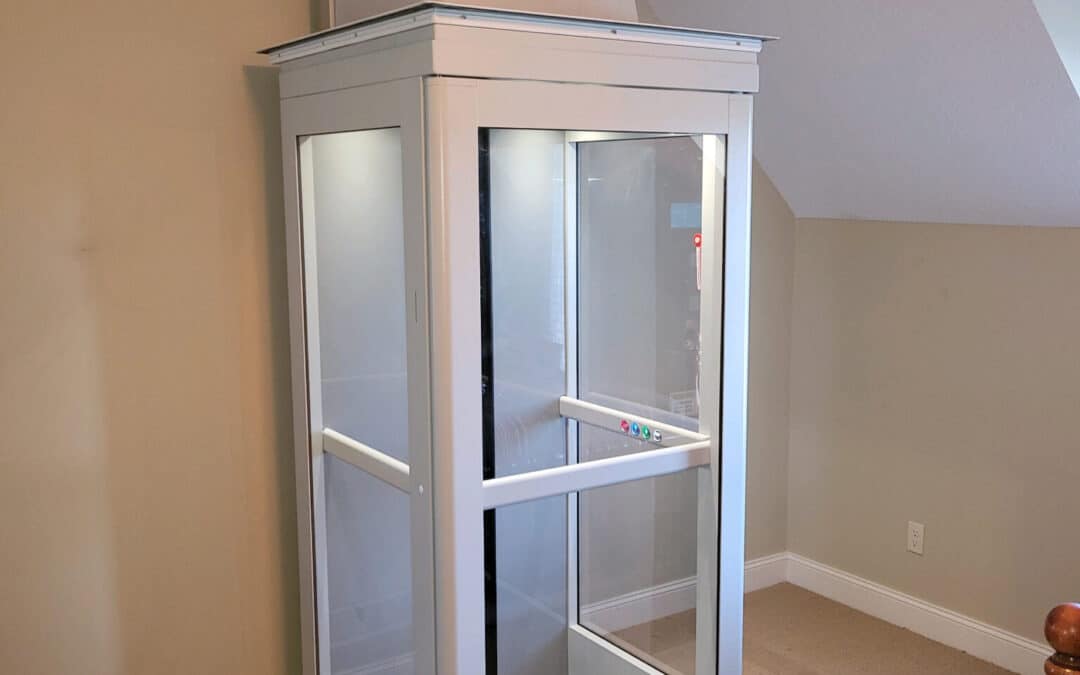 Residential glass home elevator installed in a carpeted room with angled ceilings, ready for use.