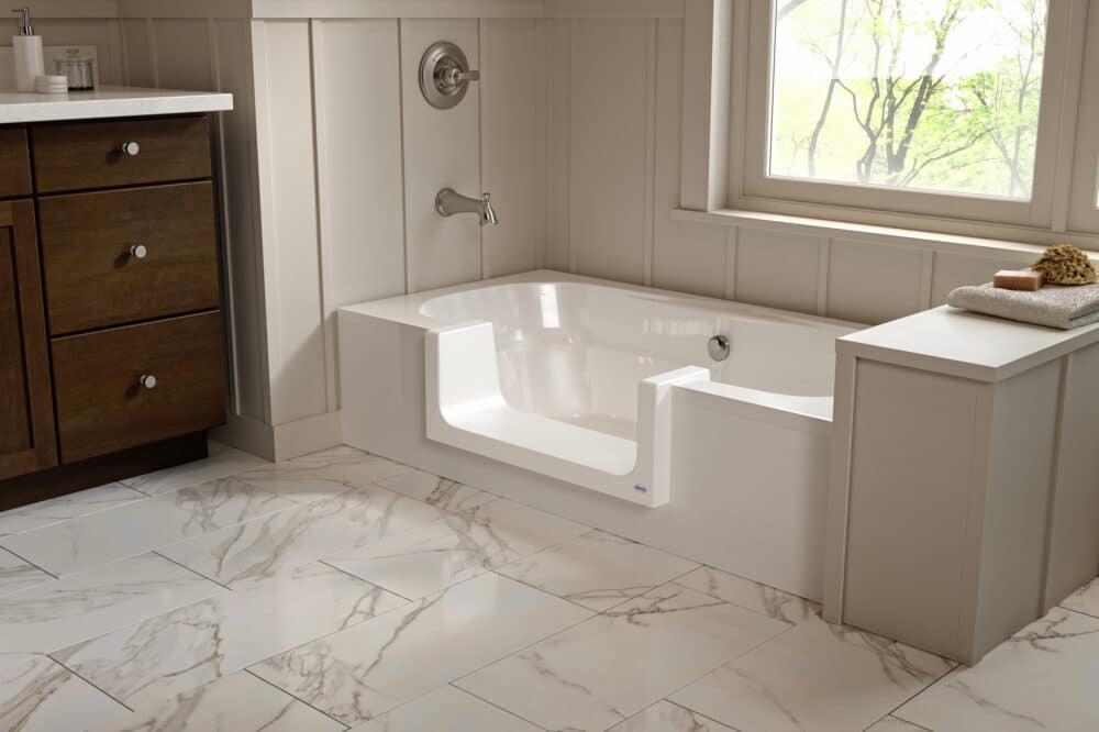 White bathtub converted with a low-step threshold and wide entry point in a marble-tiled bathroom.