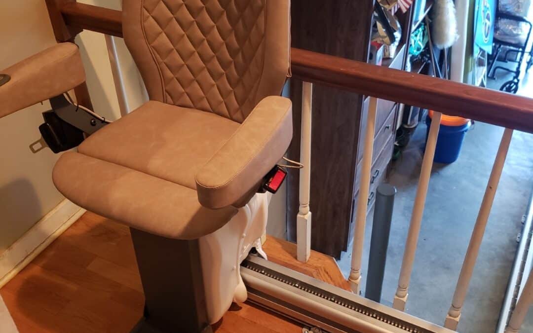 Curved stair lift with a quilted tan seat installed on a landing with wood flooring and a wooden banister.