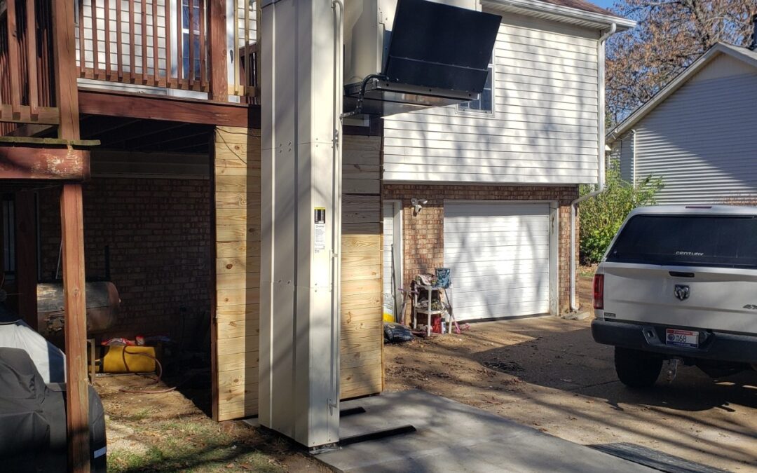 Residential outdoor vertical platform lift (VPL) installed next to a raised deck and wood-sided structure.