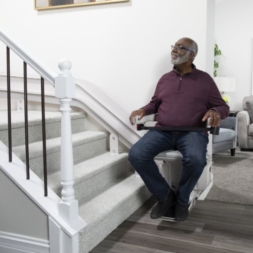 man sits in a chair lift on the wall at the bottom of the stairs in his home