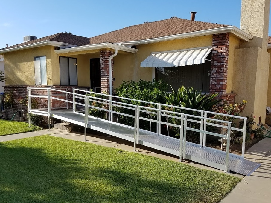 California home with blue awnings over the windows and a metal wheelchair ramp leading up to the front door.