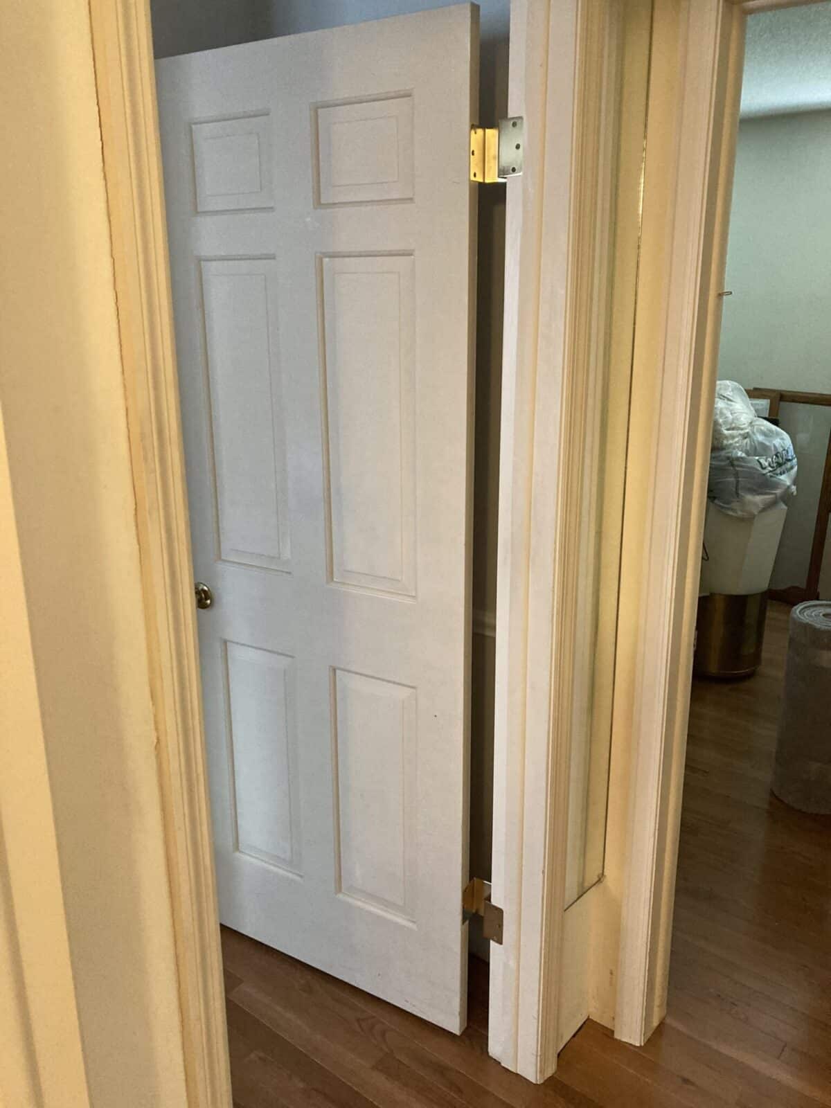 White paneled door opening outward, showing brass off-set hinges on a mirrored closet frame.