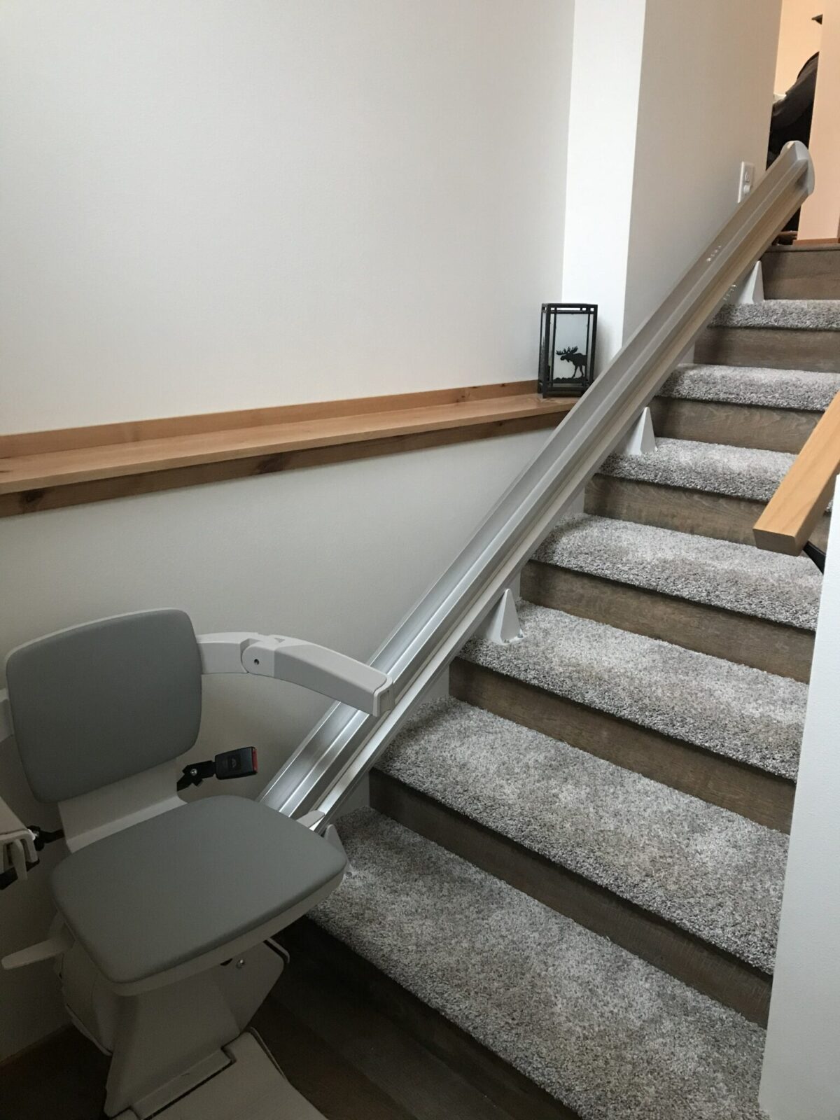 Straight stairlift with gray seat and silver rail on a speckled gray carpeted staircase.