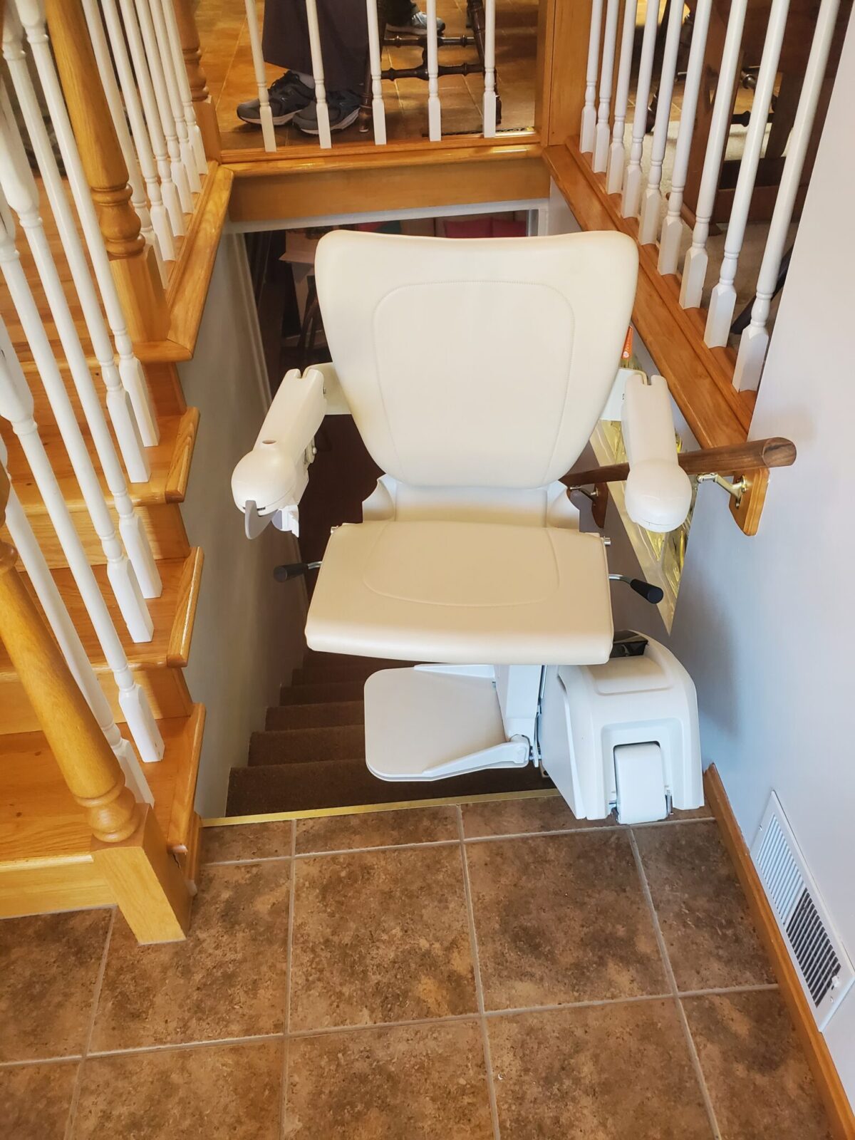 Light tan stairlift installed on straight white rail next to wooden stairs and a tiled landing.