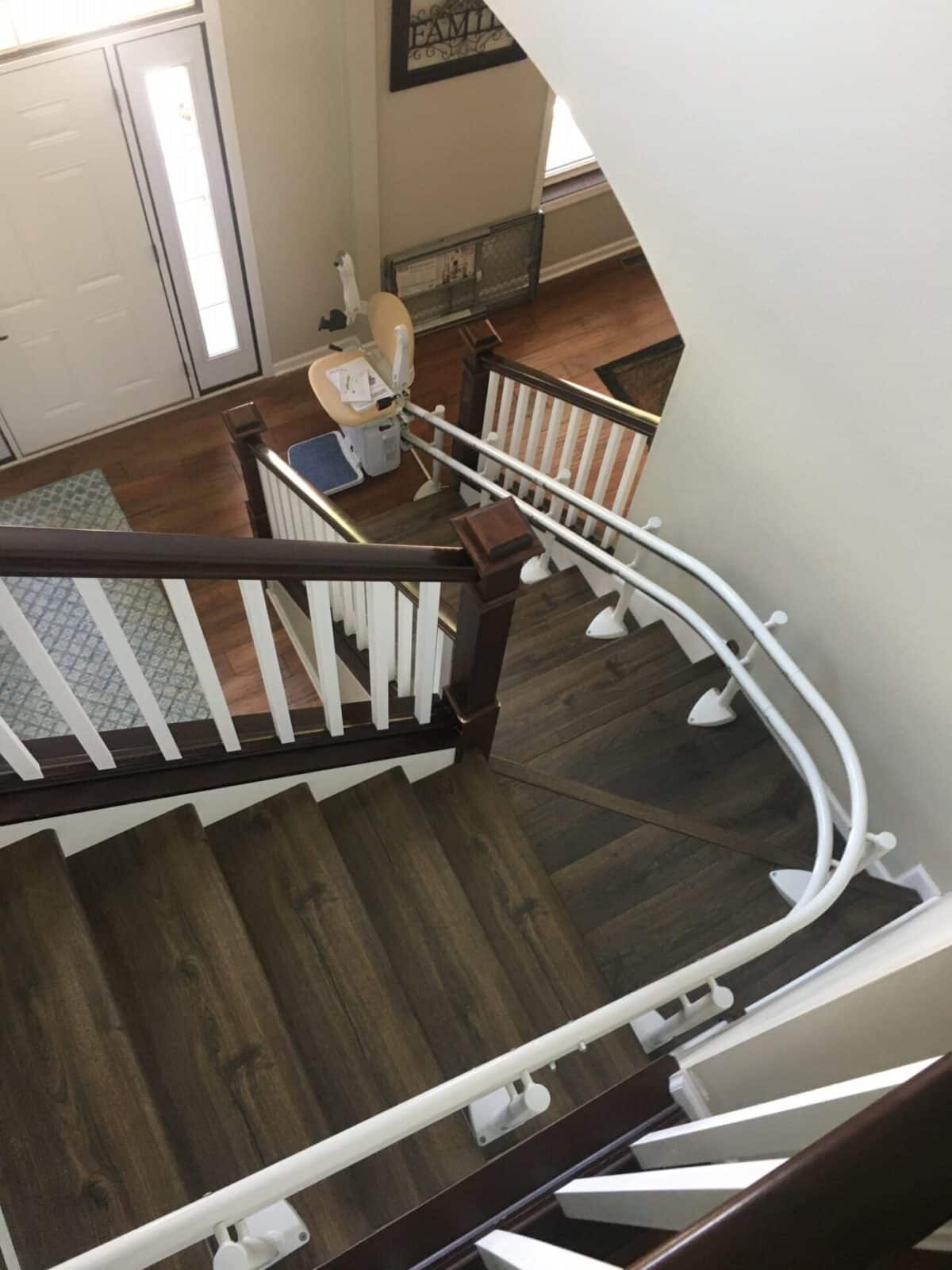 White curved rail stairlift on a dark wood staircase with white balusters.