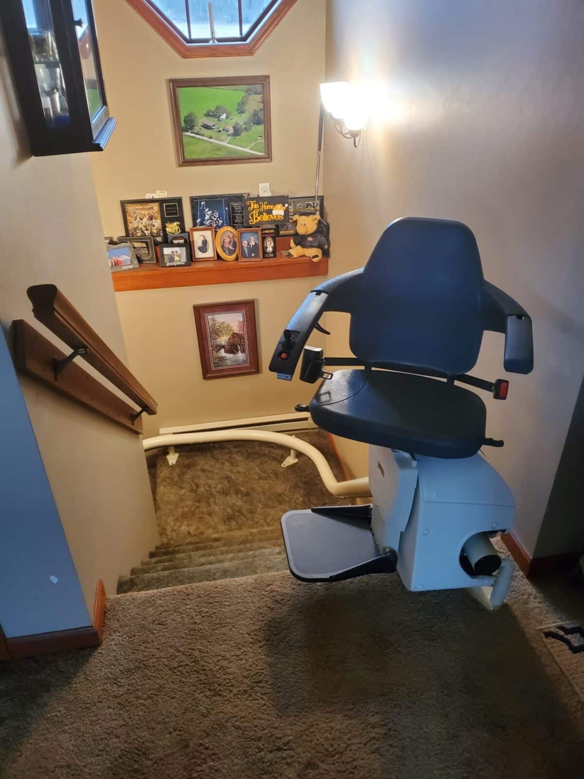 White stairlift with dark blue seat installed on a curved rail above shag carpeted stairs.