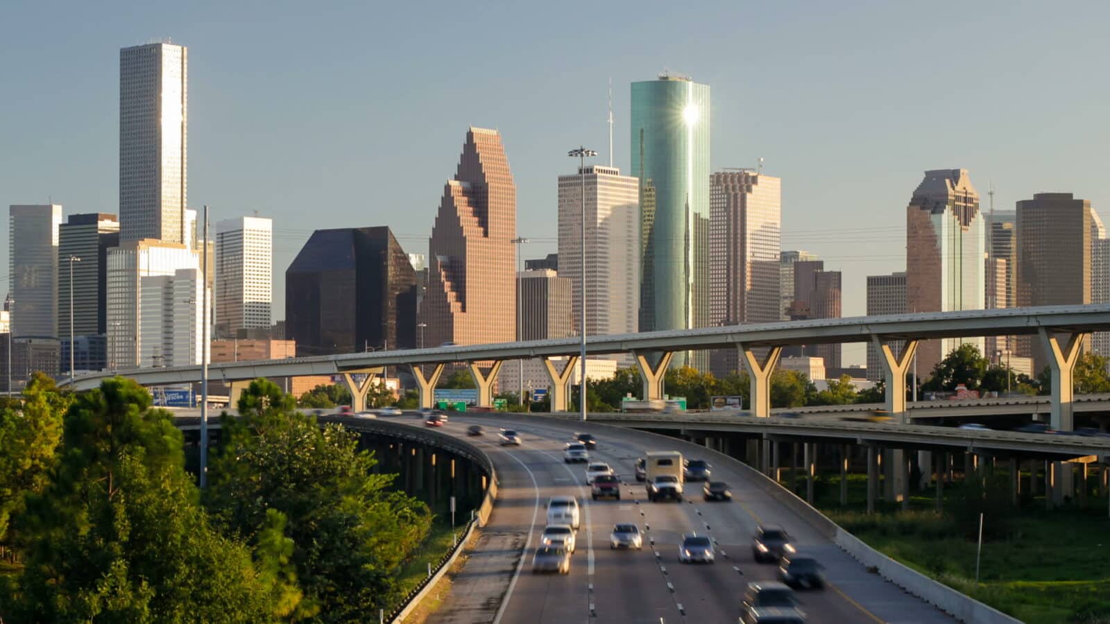 The Houston, Texas skyline at sunset, with tall downtown skyscrapers rising above a busy highway interchange.