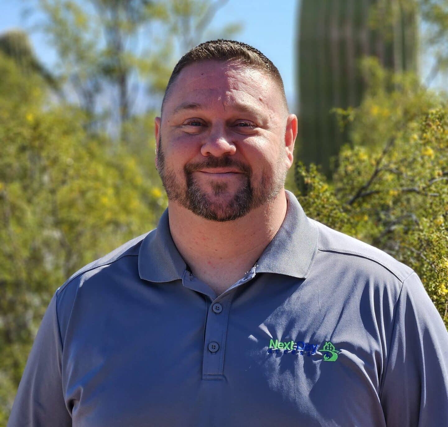 A worker in a yellow 'Next Day Access' shirt uses a power drill to assemble a ridged aluminum ramp.