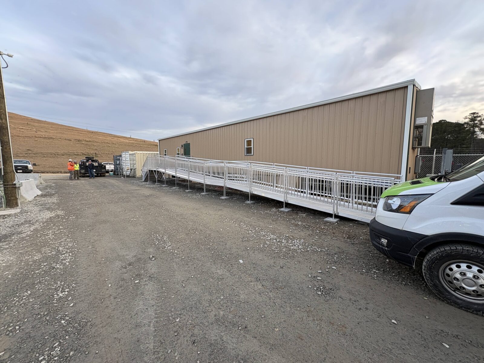 Full view of a long modular aluminum wheelchair ramp installed alongside a construction office.