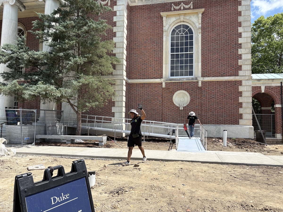 Two workers installing a modular aluminum wheelchair ramp outside a building at Duke University.