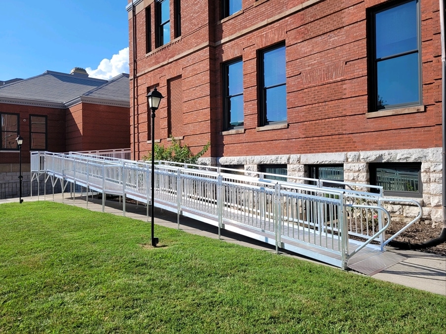 a red brick building with windows has an inclined ramp running along side a wall