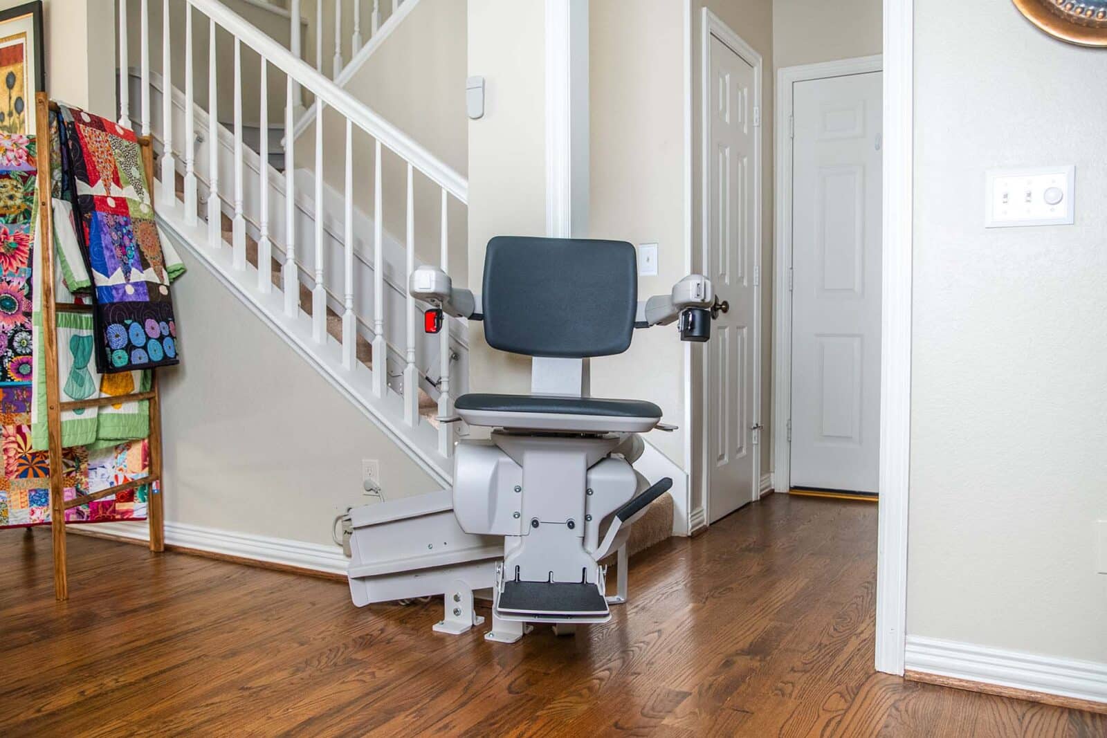 18 Curved Stairlift - 161 Glendale Dr 10202025 Woman in a blue sweater smiles and sits at the bottom of the stairs on a chair lift