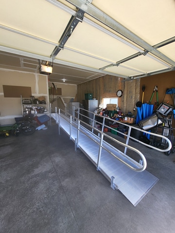 Modular aluminum wheelchair ramp with handrails installed inside a residential garage leading to an entry door