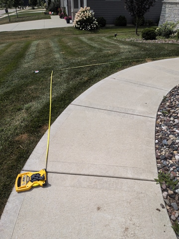 Yellow tape measure laid out along a sidewalk and lawn during an in-home wheelchair ramp assessment