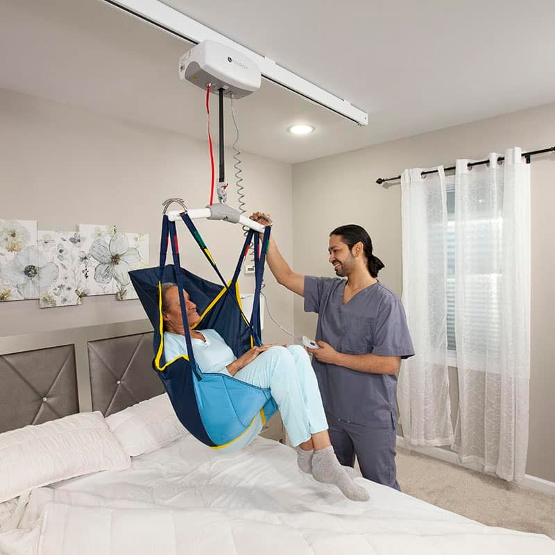 Next-Day-Access-October-Blog-17-Patient-Lifts-Create-a-Safer-Environment A nurse lowers an older woman down onto a bed using a patient lift