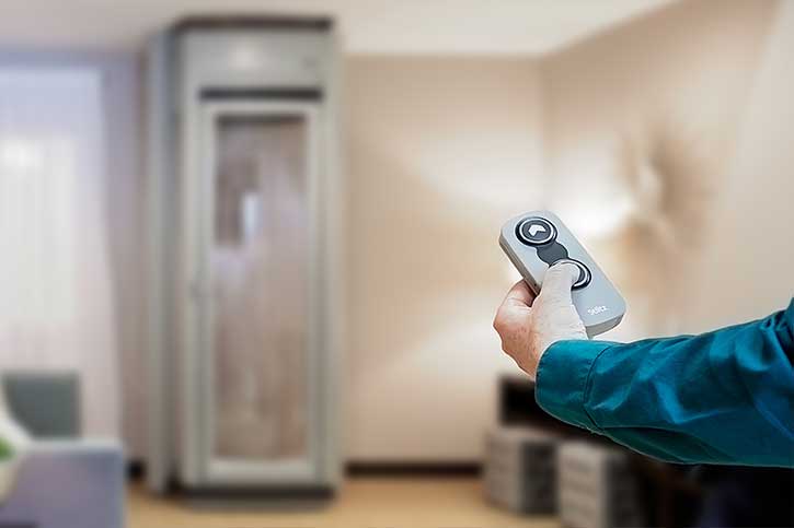 Close up of a hand holding a remote control with an in home elevator in the background