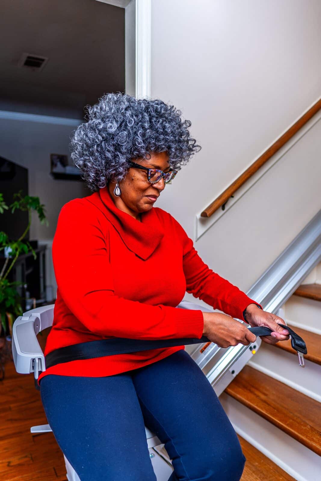 Woman in a blue sweater smiles and sits at the bottom of the stairs on a chair lift