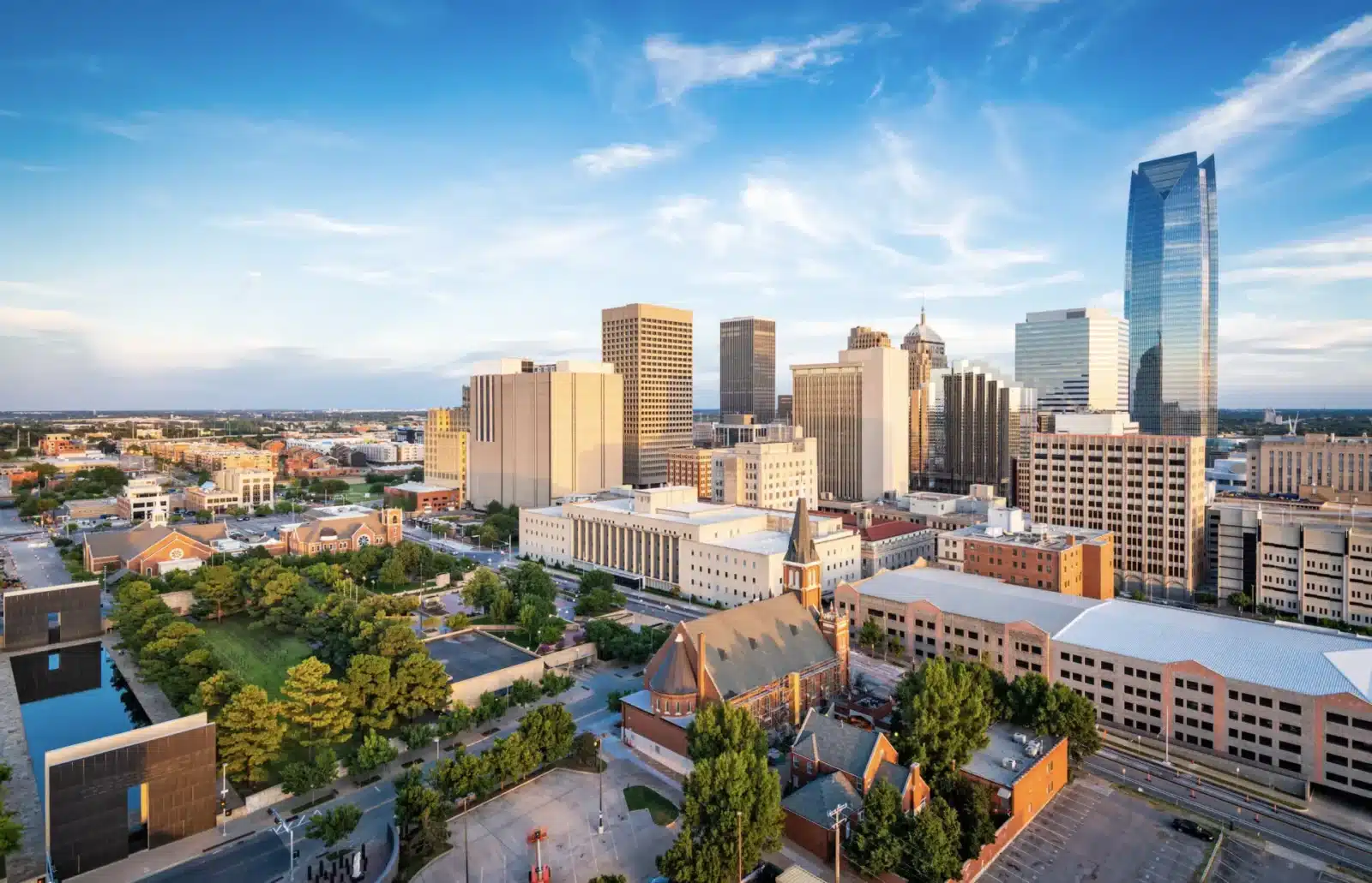 The Oklahoma City skyline at sunset, with tall buildings contrasting against the warm light and blue sky.