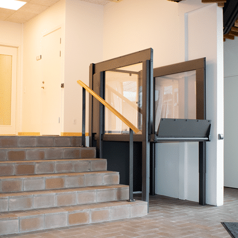 a black porch lift installed between a wall and a brown stone staircase. 