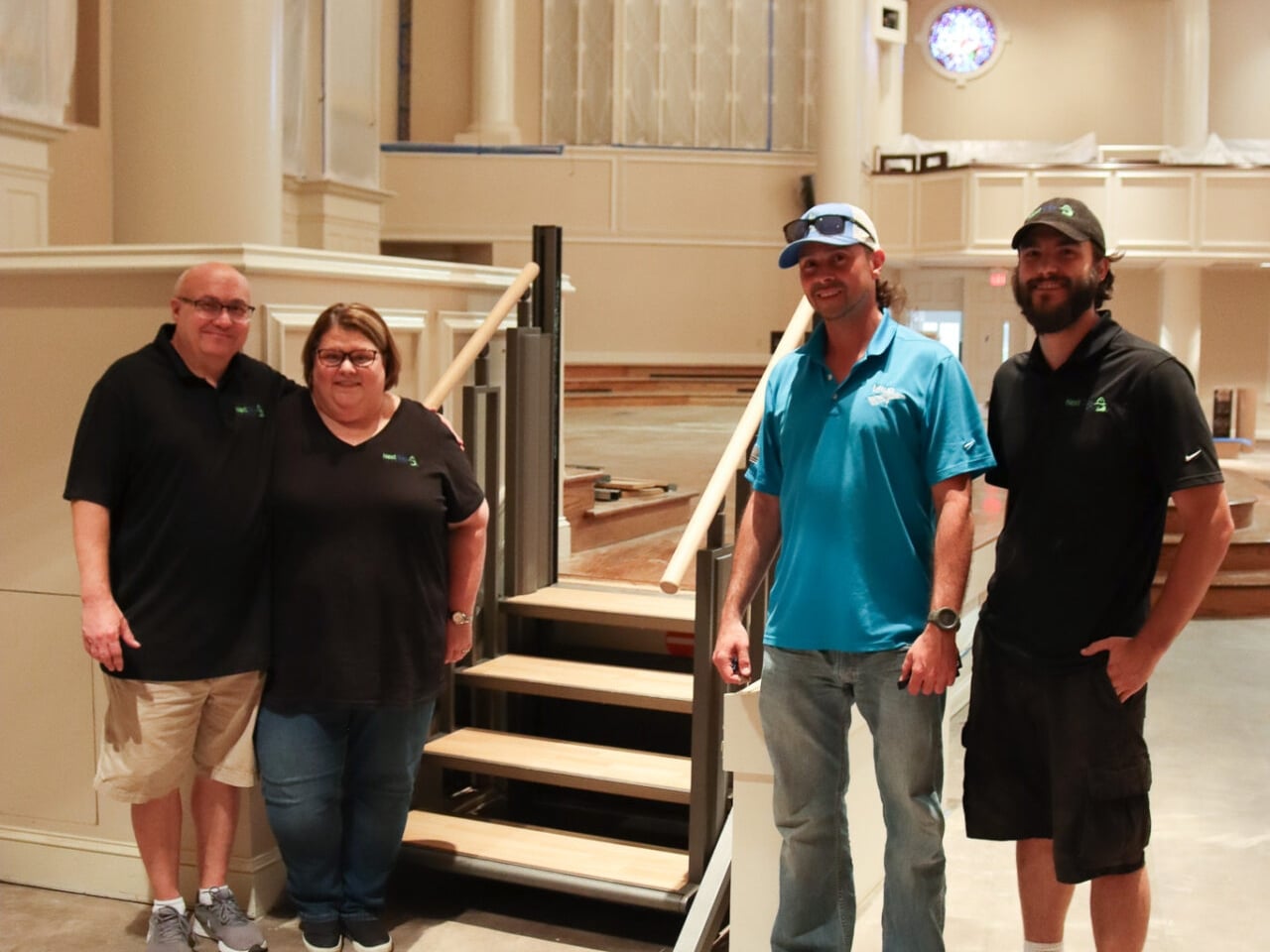 A group of four Next Day Access employees smile at the bottom of a small staircase