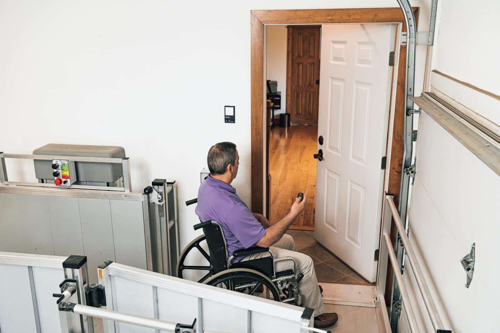 a man sits in a wheelchair opening his house door from his garage with a remote
