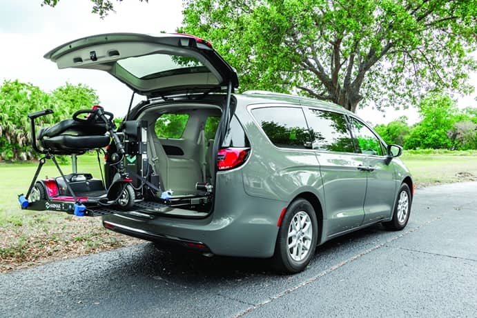 a gray minivan has its trunk open and a wheelchair platform extends from the back