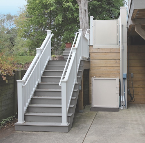 porch lift at the bottom of a very tall deck with a staircase beside it