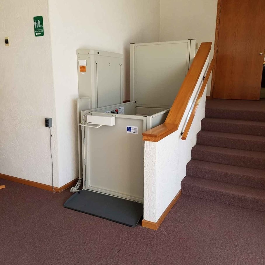 A single person wheelchair lift installed on the side of a staircase inside a business