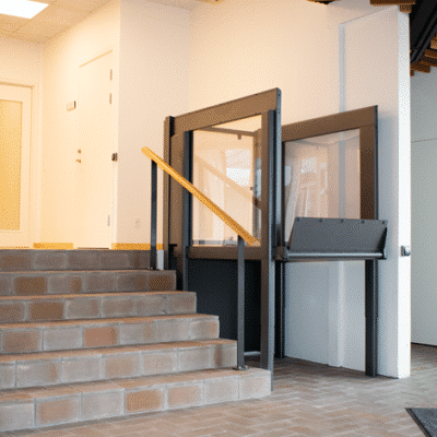 a black porch lift installed between a wall and a brown stone staircase.