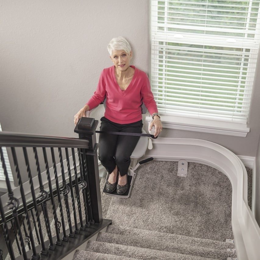 an elderly woman rides a chair lift up her home stairs