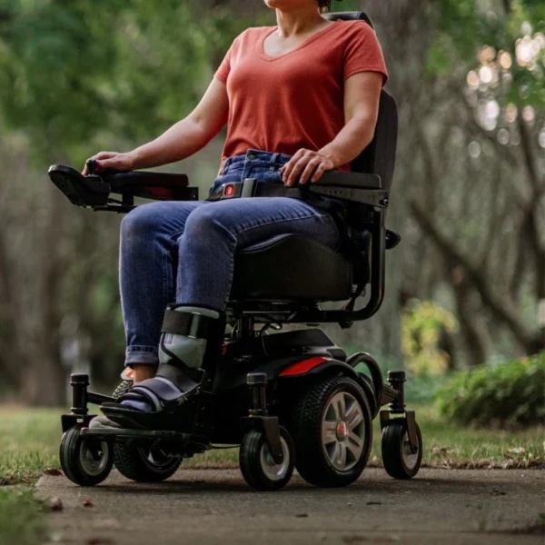 Woman rides a motorized wheelchair on a sidewalk through a forest