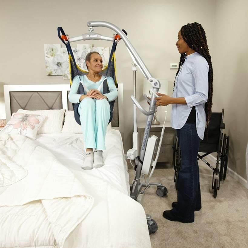 Patient sits on a lift and is lowered down into a bed by a nurse